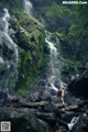 A naked woman standing in front of a waterfall.