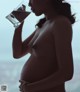 A pregnant woman drinking water from a glass.