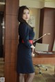 A woman in a blue dress leaning against a wooden cabinet.