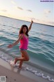 A woman in a pink tank top and denim shorts on the beach.