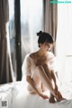 A woman sitting on top of a bed in a white dress.