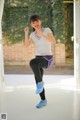 A young woman in a white shirt and black leggings doing a squat.