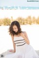 A woman in a white dress sitting on a bench on the beach.