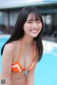 A woman in an orange bikini posing by a pool.