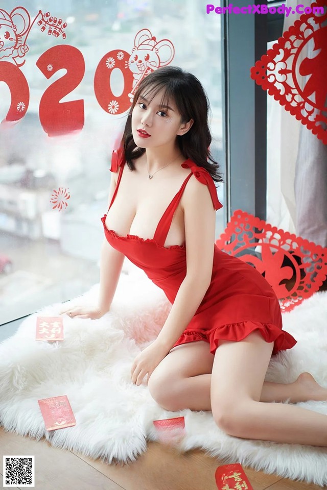 A woman in a red dress sitting on a white rug.