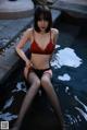 A woman in a red bra and black panties sitting in a pool.